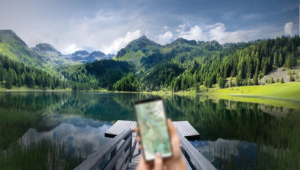 Smartphone unscharf im Vordergrund, See und Wälder scharf im Hintergrund